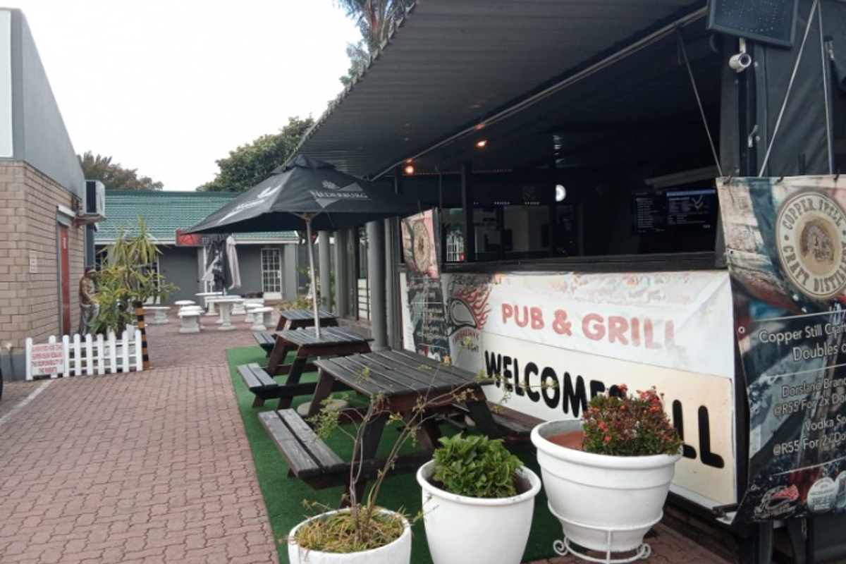 Outdoor pub and grill seating area featuring a covered bar structure, paved patio, and casual dining space.