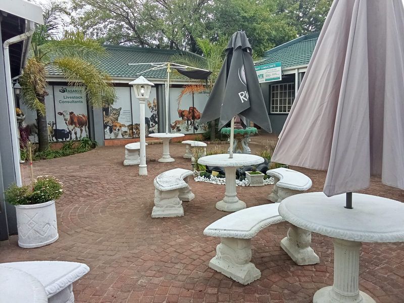 A paved outdoor courtyard area featuring built-in stone benches and tables, surrounded by commercial building facades with large window displays.