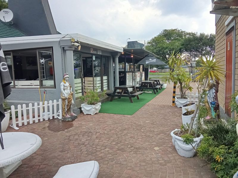 Outdoor patio area featuring paved flooring, covered seating space, and established garden planters, suitable for commercial dining or social gatherings.