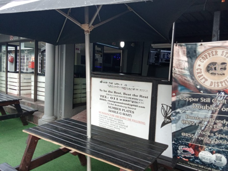 Outdoor patio area featuring a covered seating space with business signage and branding, suitable for commercial use.