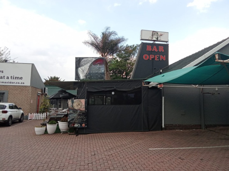 Exterior view of a commercial bar facility featuring paved parking area, signage, and covered outdoor space.