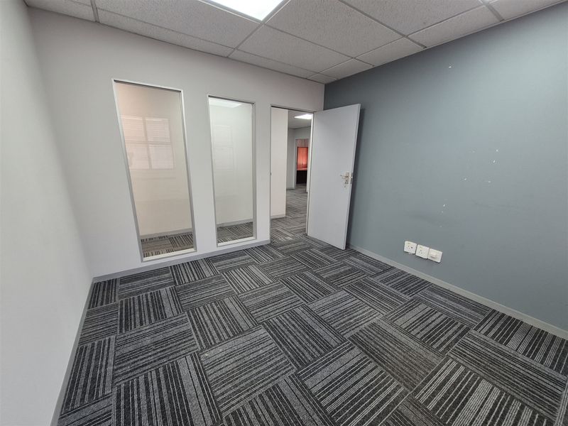 A vacant office space featuring carpet tiles, a suspended ceiling, and glass partition panels, providing a clean and functional professional environment.