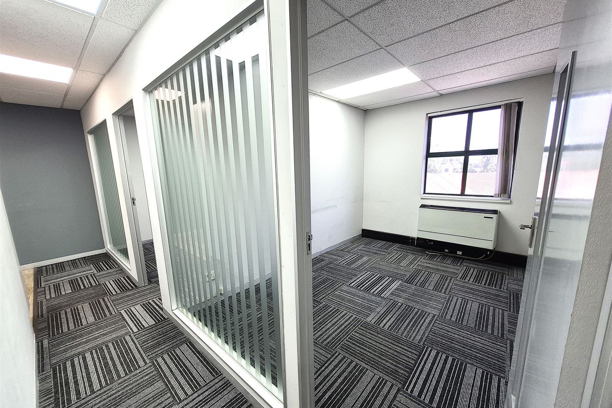 A bright, vacant office space featuring modern carpet tiles, glass partition walls, and integrated HVAC unit, suitable for a professional work environment.