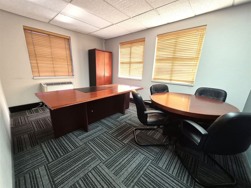 A professional office space featuring carpet tile flooring, a suspended ceiling, and large windows with venetian blinds for natural light control.