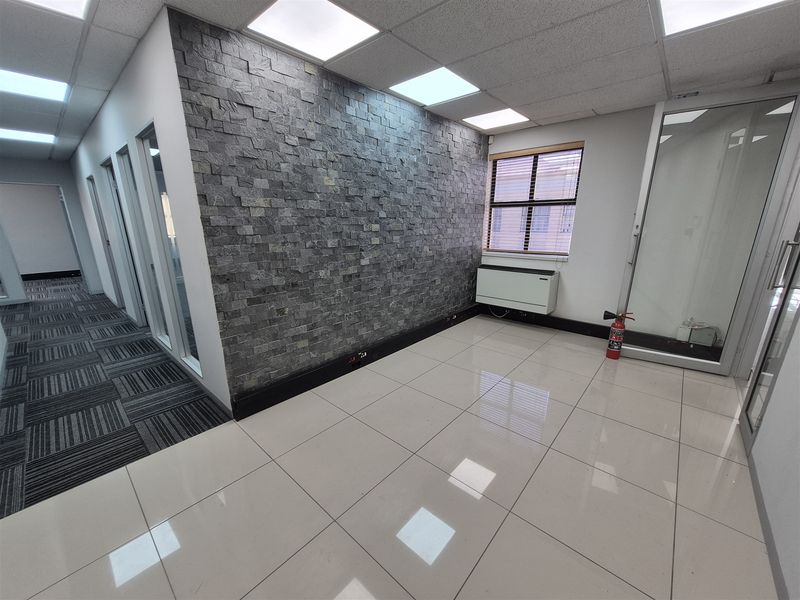 A modern, empty office space featuring a striking stone feature wall, polished tile flooring, and glass partition doors, providing a professional and bright work environment.