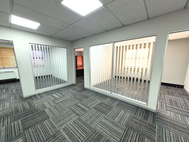 A modern, empty office space featuring glass partition walls, carpet tile flooring, and a suspended ceiling with recessed lighting.