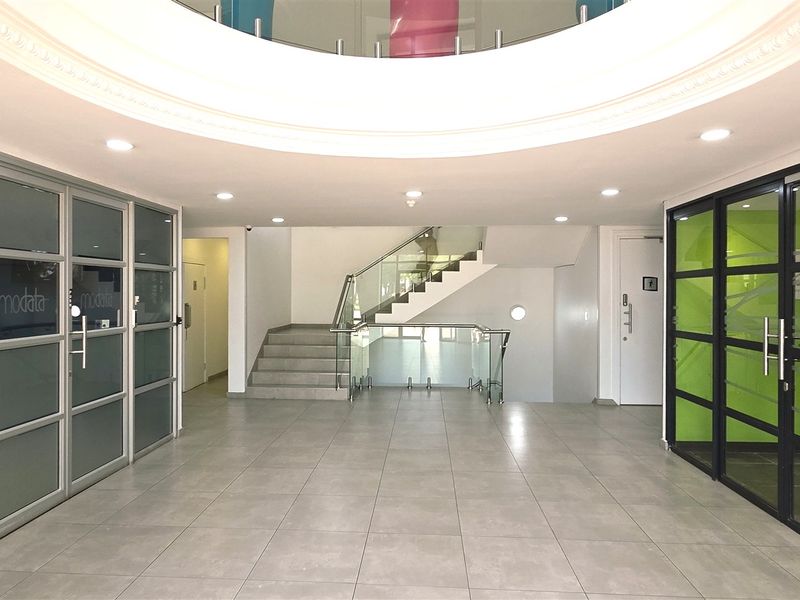 Modern office building entrance lobby featuring tiled flooring, glass partition walls, and a central staircase with a glass balustrade.