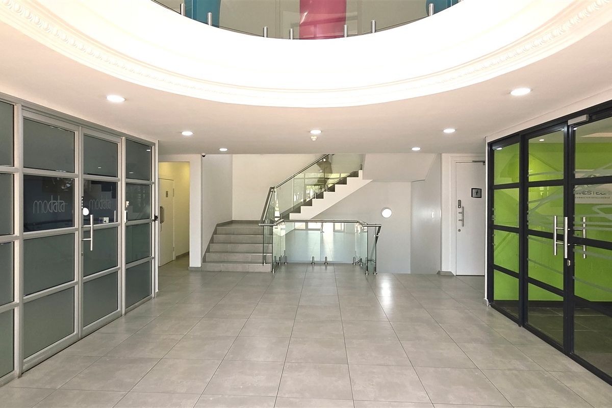 Modern office building entrance lobby featuring tiled flooring, glass partition walls, and a central staircase with a glass balustrade.
