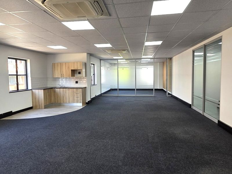 Spacious open-plan office area featuring a modern kitchenette, glass-partitioned meeting rooms, suspended ceilings with recessed lighting, and integrated cassette air conditioning.