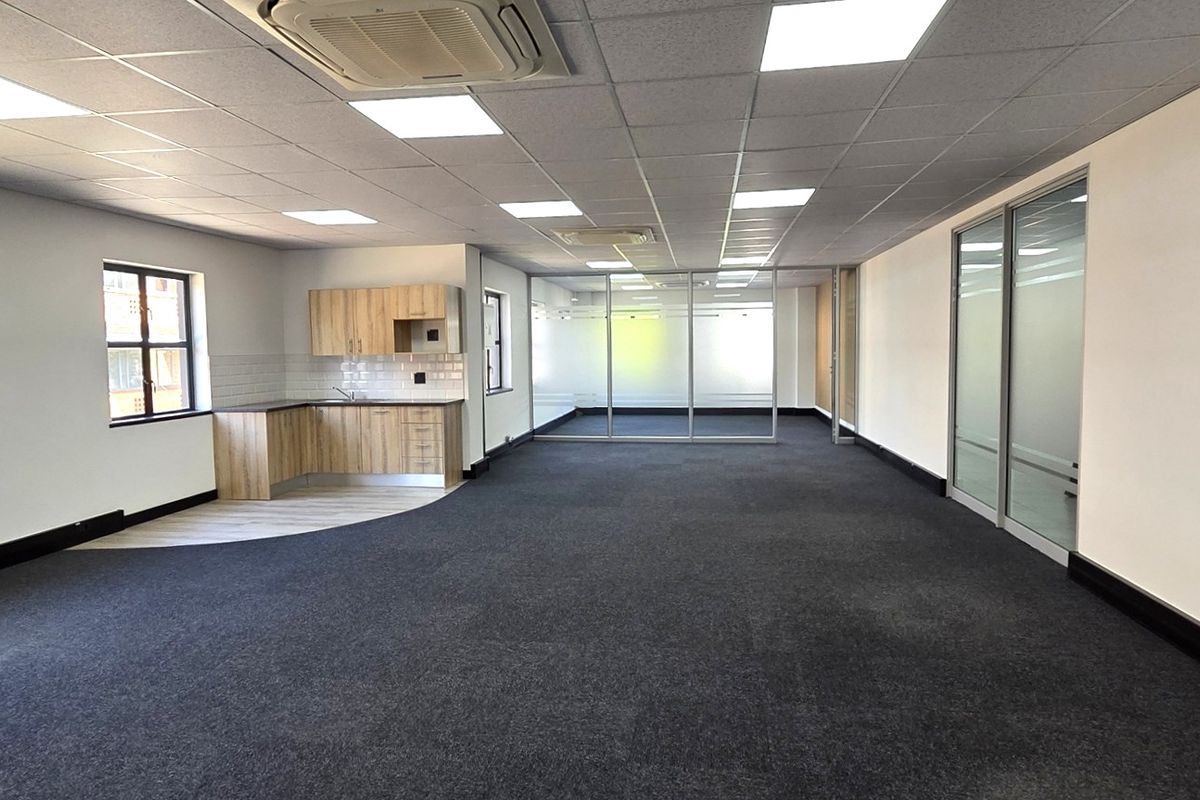 Spacious open-plan office area featuring a modern kitchenette, glass-partitioned meeting rooms, suspended ceilings with recessed lighting, and integrated cassette air conditioning.