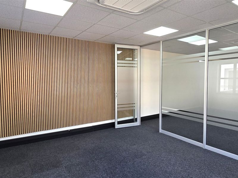 Modern office space featuring a striking slatted timber feature wall, glass partitioning, recessed LED lighting, and clean carpet flooring.