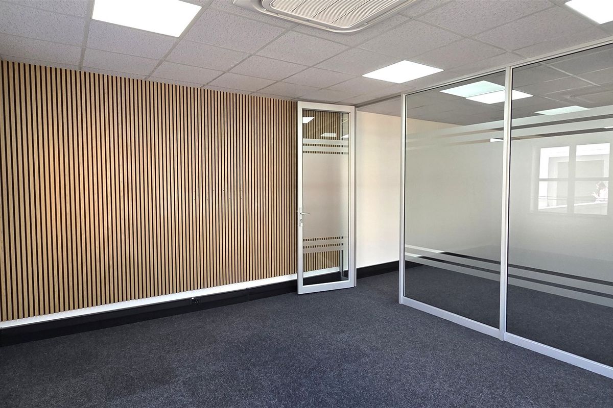 Modern office space featuring a striking slatted timber feature wall, glass partitioning, recessed LED lighting, and clean carpet flooring.