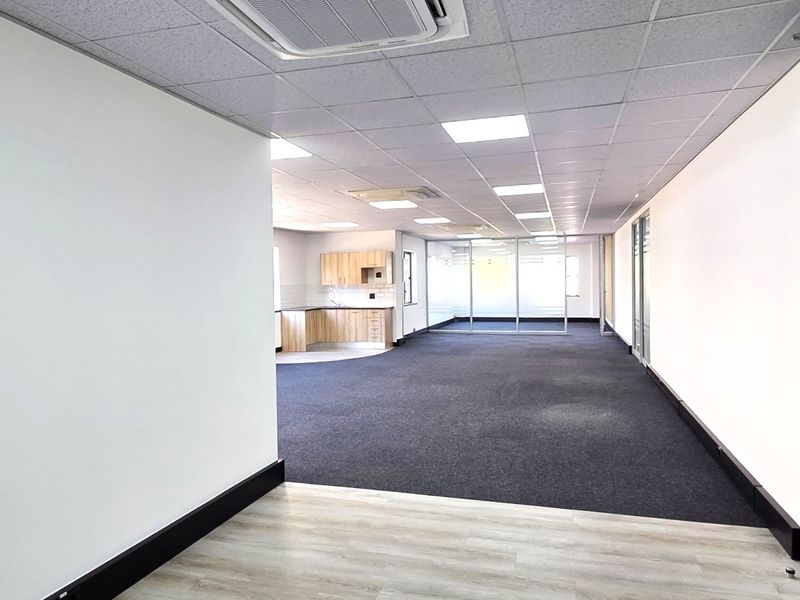 Spacious open-plan office area featuring a suspended ceiling, recessed lighting, integrated air conditioning, glass partitions, and a small kitchenette.