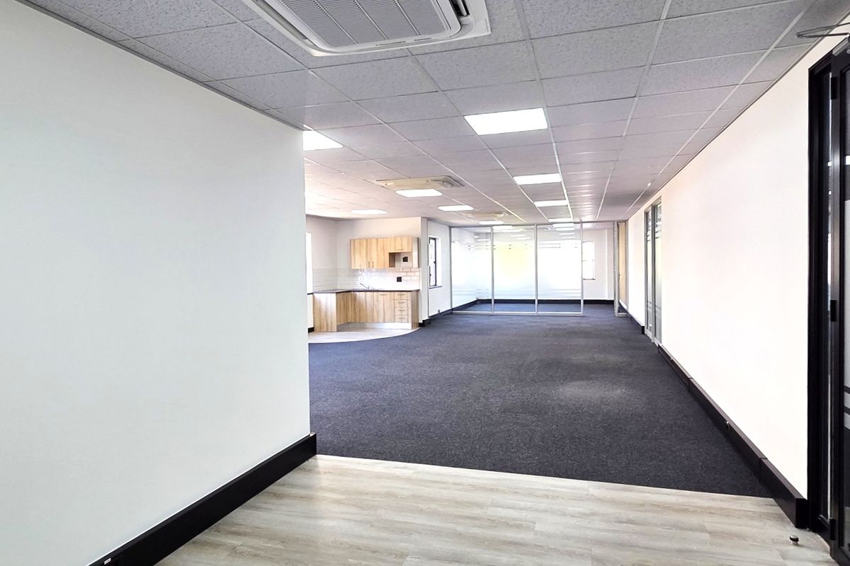 Spacious open-plan office area featuring a suspended ceiling, recessed lighting, integrated air conditioning, glass partitions, and a small kitchenette.