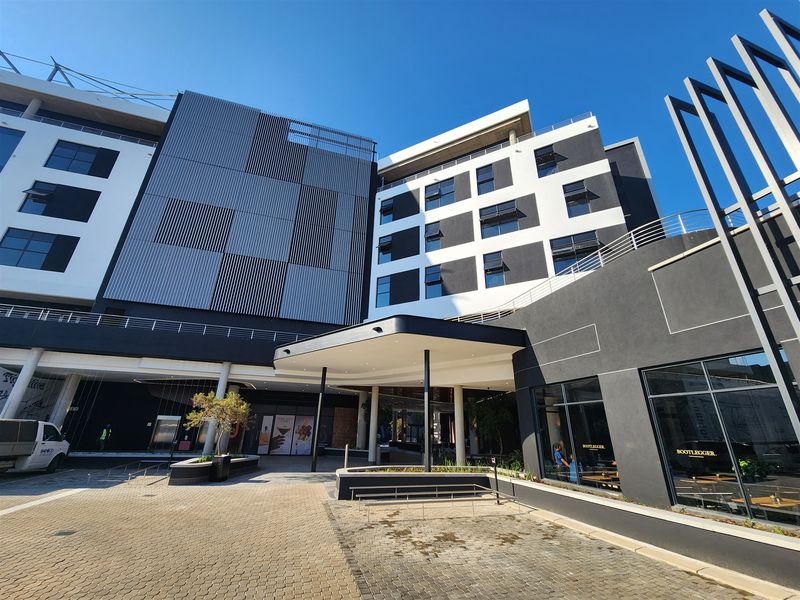 Modern multi-story office building exterior featuring a prominent entrance canopy, contemporary facade design, and large glass storefronts at street level.