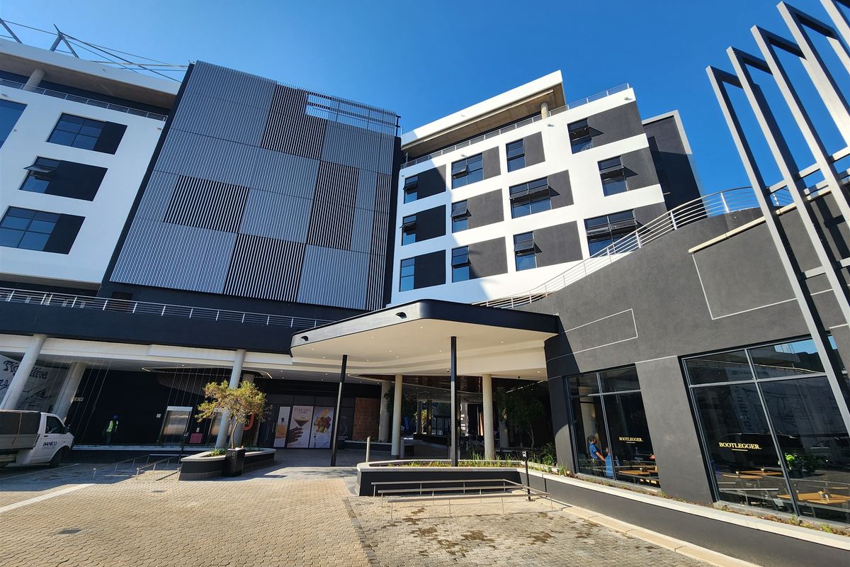Modern multi-story office building exterior featuring a prominent entrance canopy, contemporary facade design, and large glass storefronts at street level.