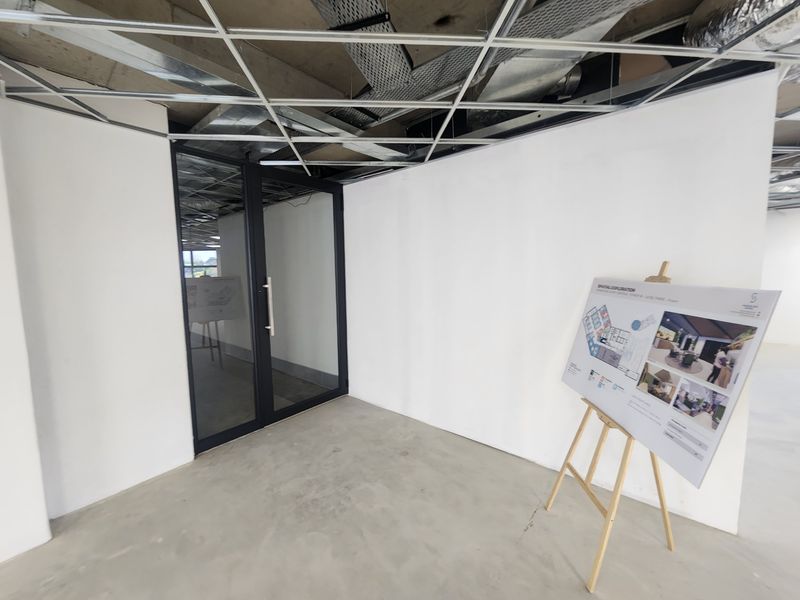 An unfinished office space featuring exposed ceiling infrastructure, a modern glass partition door, and concrete flooring, ready for final fit-out.