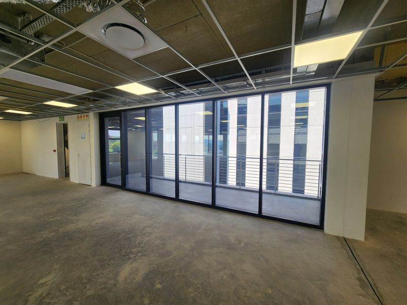 Open-plan office space featuring an unfinished ceiling, concrete flooring, and large glass sliding doors leading to a private balcony.