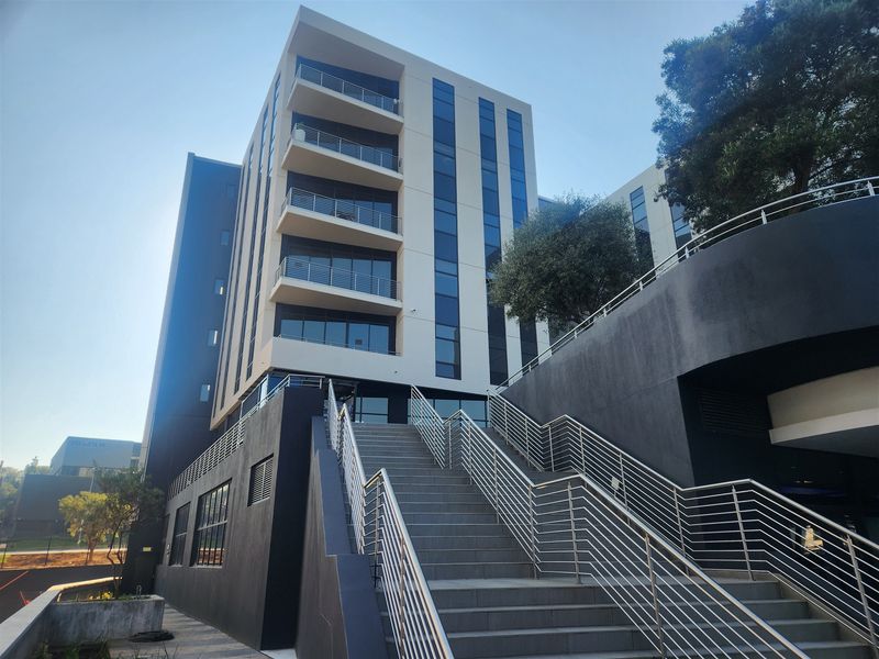 Modern multi-story office building featuring a prominent external staircase, glass facade, and integrated balconies with stainless steel railings.