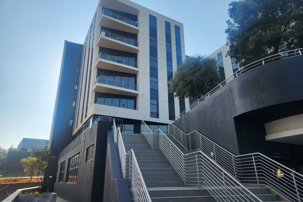 Modern multi-story office building featuring a prominent external staircase, glass facade, and integrated balconies with stainless steel railings.