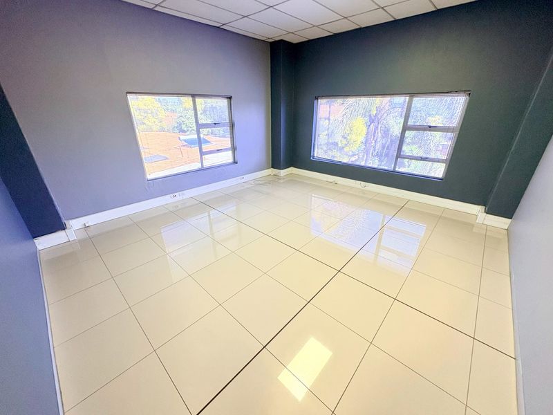 A bright, empty office space featuring large windows, modern tiled flooring, and a suspended ceiling, offering a clean and professional work environment.