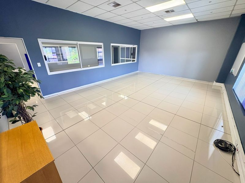 A spacious, empty office area featuring polished tiled flooring, a suspended ceiling with recessed lighting, and large sliding windows.