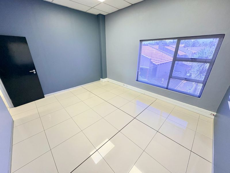 A clean, empty office space featuring polished tiled flooring, a suspended ceiling, and a large window providing natural light.