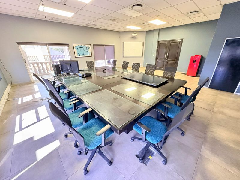 A functional office boardroom featuring tiled flooring, a suspended ceiling with recessed lighting, and direct access to an outdoor balcony area.