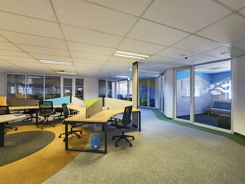 Modern open-plan office space featuring glass-partitioned meeting rooms, suspended ceilings with recessed lighting, and durable carpet flooring.