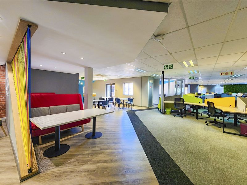 Modern open-plan office space featuring a mix of laminate and carpet flooring, suspended ceilings with recessed lighting, and designated collaborative work zones.