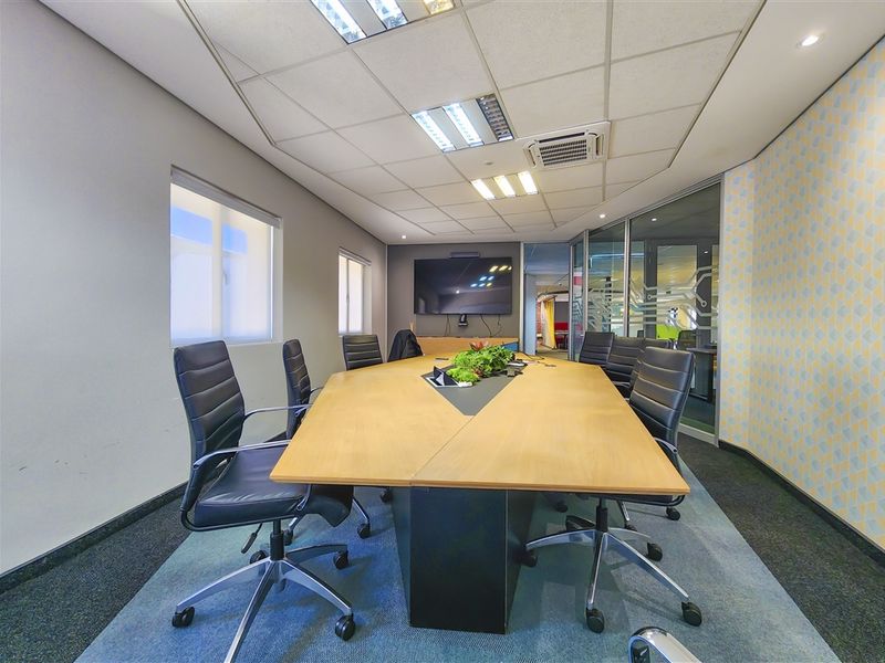 A professional office boardroom featuring a large central table, glass partition walls, suspended ceiling with recessed lighting, and integrated air conditioning.