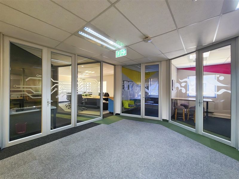 Modern office space featuring glass partition walls, suspended ceilings with recessed lighting, and carpeted flooring, creating a professional and open work environment.