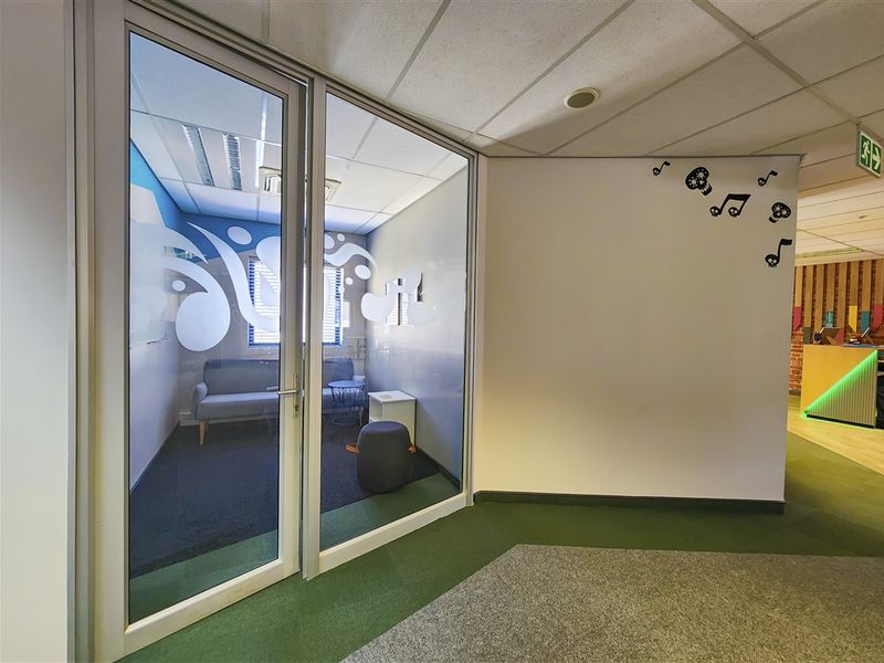 A modern office space featuring a glass-partitioned meeting room with carpet flooring and a suspended ceiling in a professional commercial environment.