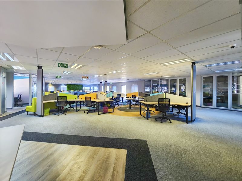 Spacious open-plan office area featuring a mix of carpet and laminate flooring, suspended ceilings with recessed lighting, and modern glass partitioning.