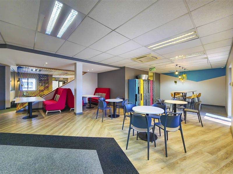 A modern, open-plan office breakout area featuring laminate flooring, suspended ceilings with recessed lighting, and integrated storage lockers.