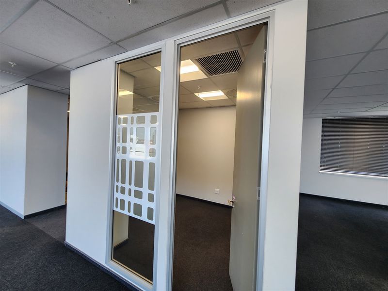 A vacant office space featuring a glass partition, suspended ceiling with recessed lighting, air conditioning, and dark carpet flooring.