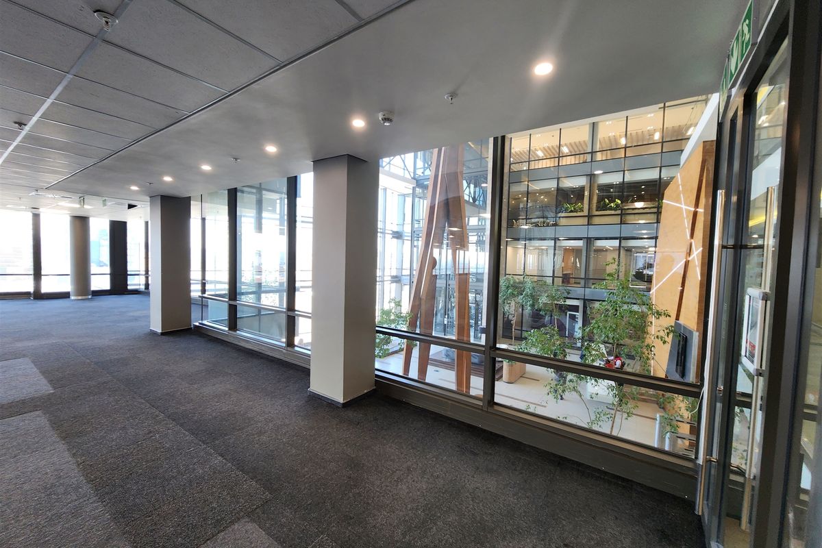 Spacious, modern office corridor featuring extensive glass partitioning, suspended ceilings with recessed lighting, and views into the building's central atrium.