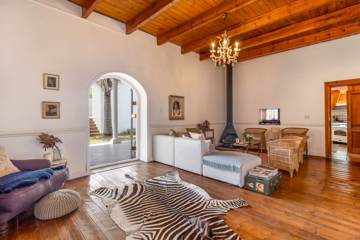 Spacious living room featuring exposed timber beam ceilings, hardwood flooring, a built-in fireplace, and an arched doorway leading to an outdoor patio area.