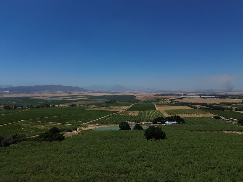 Expansive aerial view of the farm property, showcasing vast cultivated fields, orchards, and a private dam set against a scenic mountain backdrop.