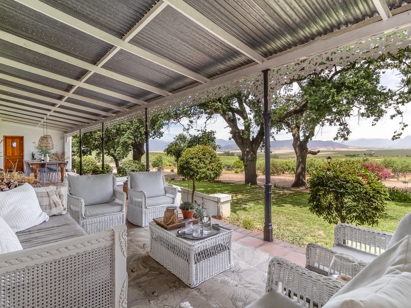 Spacious covered patio featuring decorative ironwork, corrugated metal roofing, and expansive views over the farm landscape and surrounding orchards.