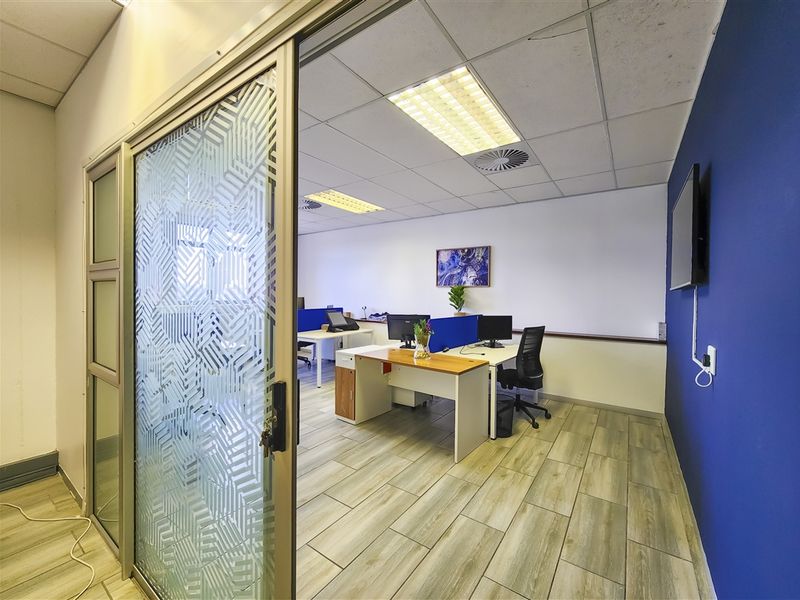 A modern office space featuring wood-look tile flooring, a suspended ceiling with recessed lighting, and a decorative sliding glass entrance door.