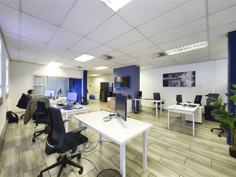 A spacious open-plan office area featuring modern tiled flooring, a suspended ceiling with integrated lighting, and air conditioning vents.