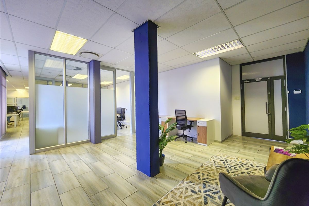 Modern office space featuring glass partitions, suspended ceilings with recessed lighting, and durable tiled flooring, creating a professional and bright work environment.