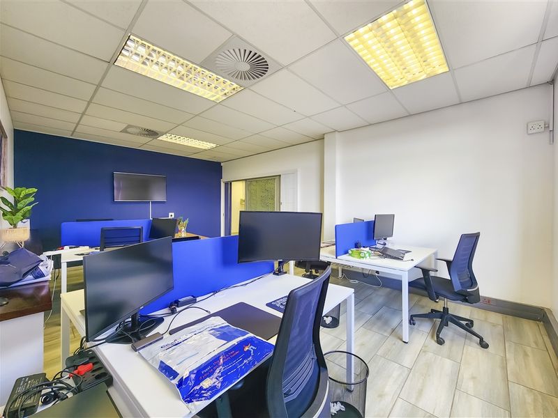 A functional office space featuring tiled flooring, a suspended ceiling with recessed lighting, and integrated air conditioning, configured with multiple workstations.