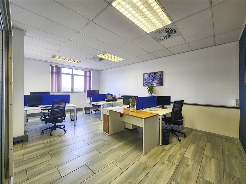 A well-maintained open-plan office space featuring wood-look tile flooring, suspended ceilings with recessed lighting, and integrated air conditioning.