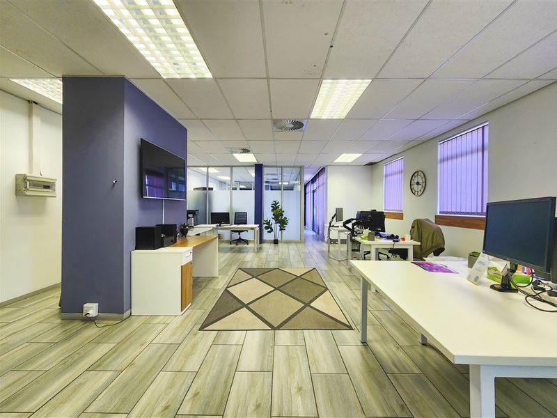 A modern open-plan office space featuring wood-look flooring, suspended ceilings with recessed lighting, and glass partitions for a professional, bright working environment.