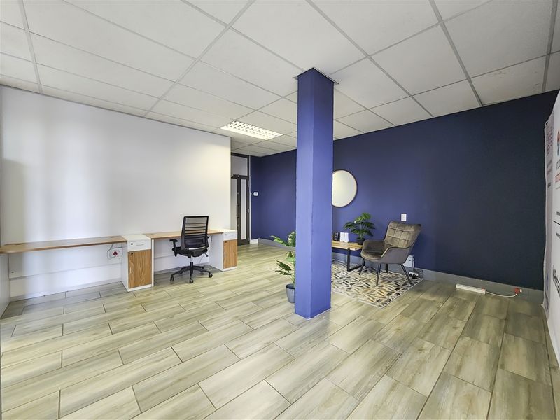 A modern office space featuring wood-look tile flooring, a suspended ceiling with recessed lighting, and a functional built-in desk area.