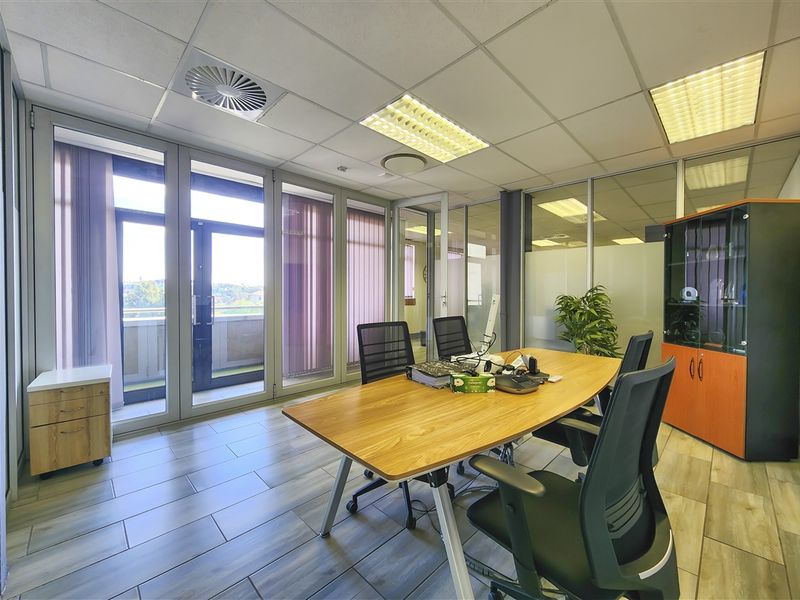 A professional office space featuring glass partition walls, suspended ceilings with recessed lighting, and direct access to an outdoor balcony area.