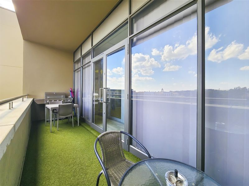 A covered balcony featuring artificial grass flooring, metal railings, and large glass sliding doors providing access to the interior office space.