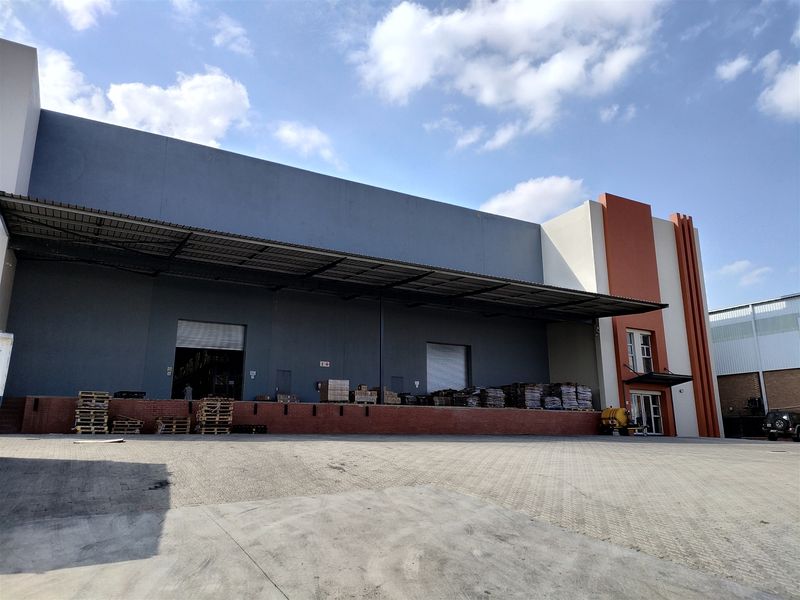 Industrial warehouse exterior featuring a large paved loading yard, covered loading dock area, and modern facade with roller shutter access points.